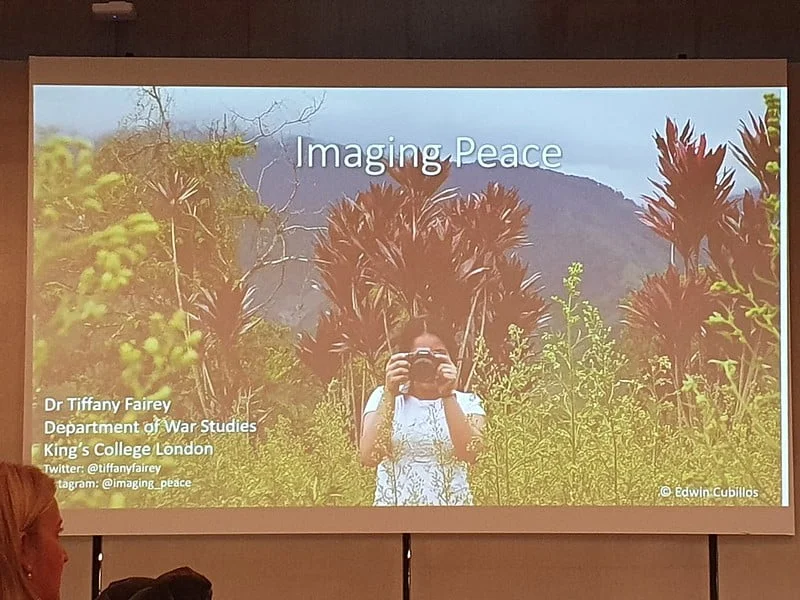 Slide showing a woman looking through a camera in a forest setting and the title 'Imagining Peace'. There is also text reading Dr Tiffany Fairey, Department of War Studies, Kings College London